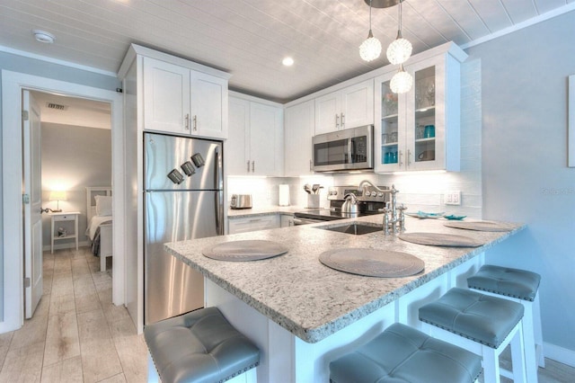 kitchen with a kitchen bar, appliances with stainless steel finishes, white cabinets, hanging light fixtures, and light stone counters