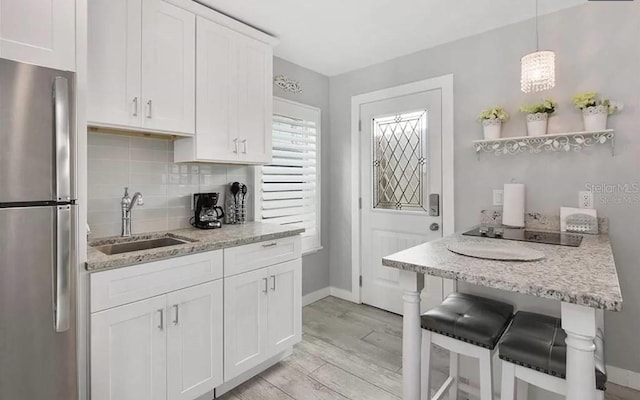 kitchen featuring decorative light fixtures, stainless steel fridge, sink, and white cabinetry