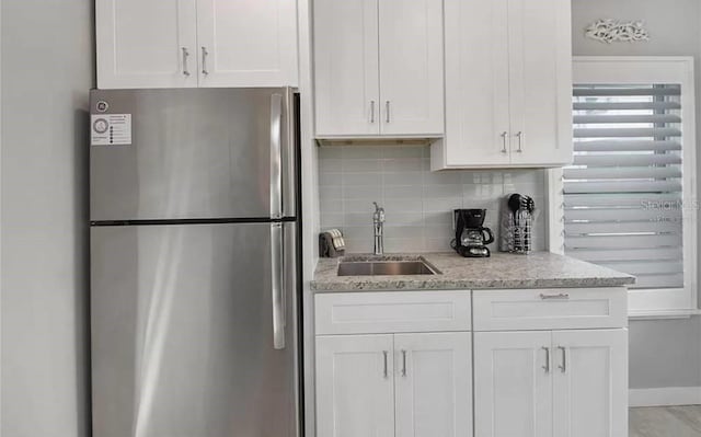 kitchen with light stone countertops, white cabinetry, tasteful backsplash, sink, and stainless steel fridge