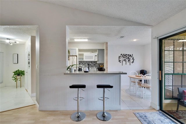 kitchen featuring gray cabinetry, a kitchen breakfast bar, light hardwood / wood-style floors, kitchen peninsula, and white appliances