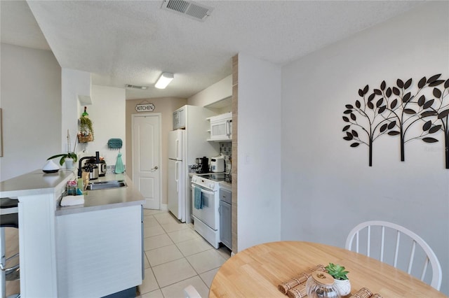 kitchen with light tile patterned flooring, white appliances, a textured ceiling, and white cabinets