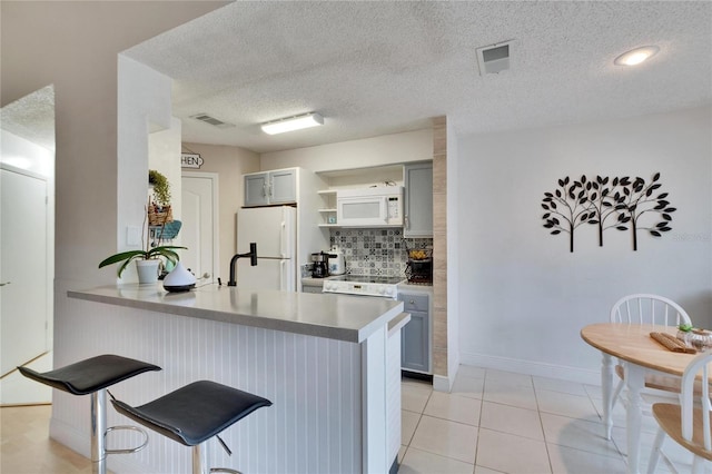 kitchen with gray cabinets, light tile patterned flooring, a kitchen breakfast bar, kitchen peninsula, and white appliances