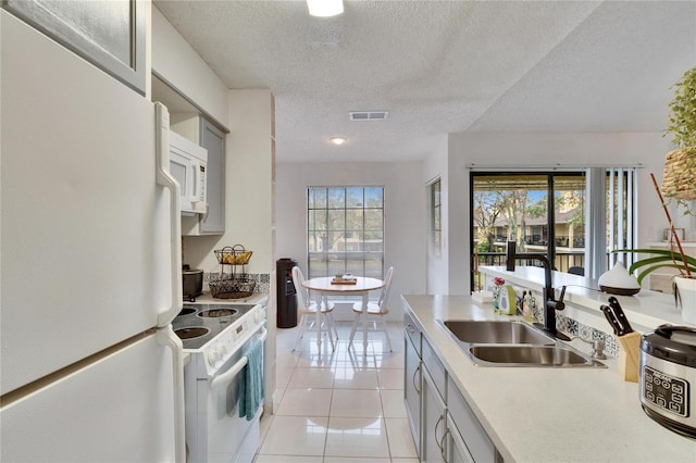 kitchen with sink, white appliances, light tile patterned floors, and a healthy amount of sunlight