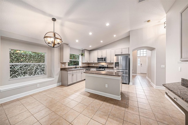 kitchen with lofted ceiling, light tile patterned floors, sink, stainless steel appliances, and a center island