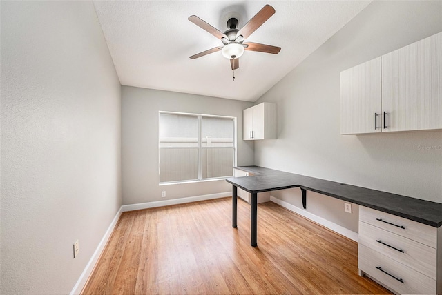 unfurnished office featuring ceiling fan, lofted ceiling, built in desk, and light wood-type flooring