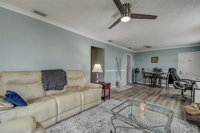 living room featuring wood-type flooring, a textured ceiling, ceiling fan, and ornamental molding