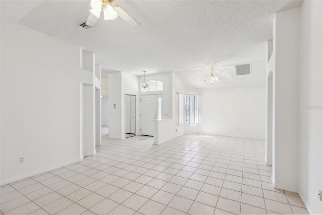 tiled empty room featuring lofted ceiling, ceiling fan with notable chandelier, and a textured ceiling