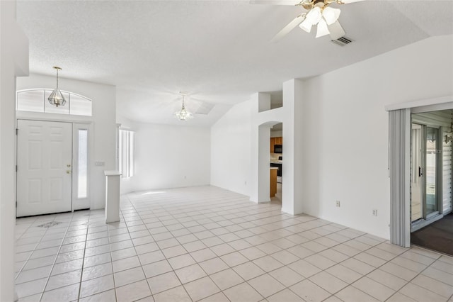 tiled entryway featuring ceiling fan with notable chandelier, vaulted ceiling, and a textured ceiling