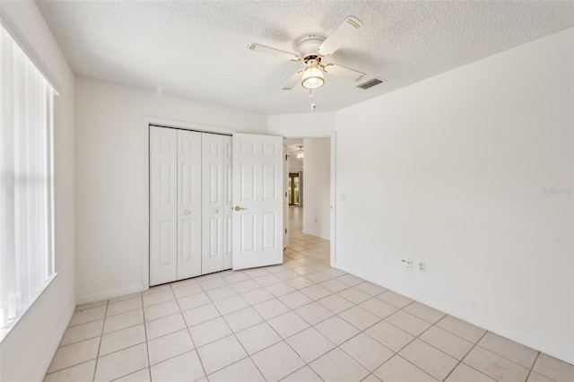 unfurnished bedroom with ceiling fan, light tile patterned floors, a closet, and a textured ceiling