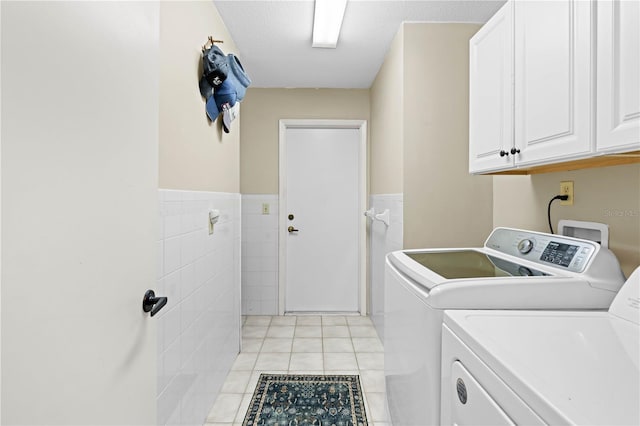 clothes washing area featuring washing machine and clothes dryer, cabinets, a textured ceiling, tile walls, and light tile patterned floors