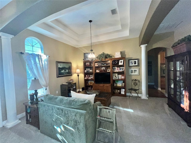 living room with decorative columns, a raised ceiling, and carpet