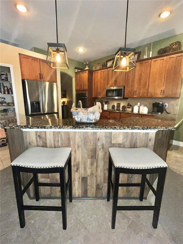 kitchen with appliances with stainless steel finishes, a breakfast bar area, hanging light fixtures, and dark stone countertops