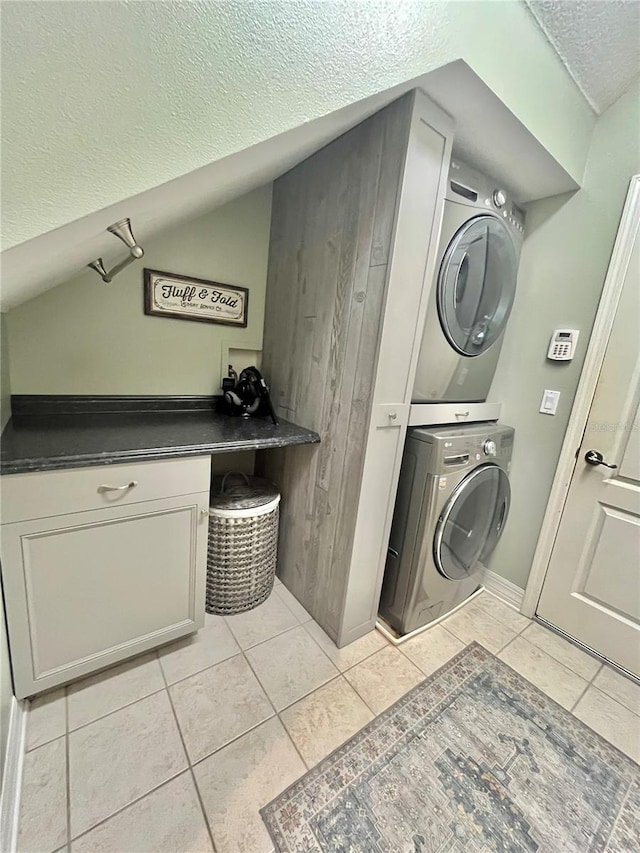 clothes washing area with stacked washer / drying machine, light tile patterned floors, cabinets, and a textured ceiling