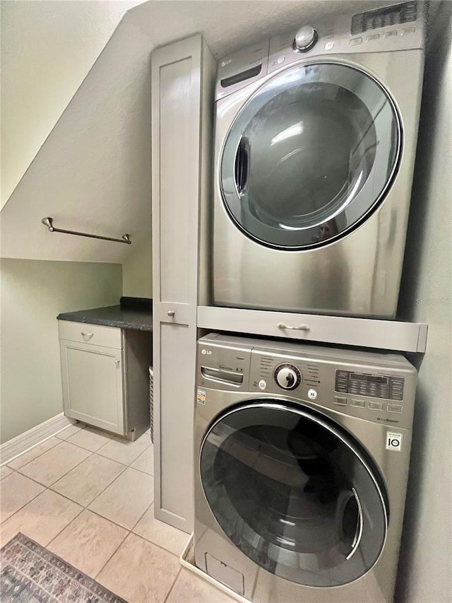 washroom featuring cabinets, stacked washing maching and dryer, and light tile patterned floors