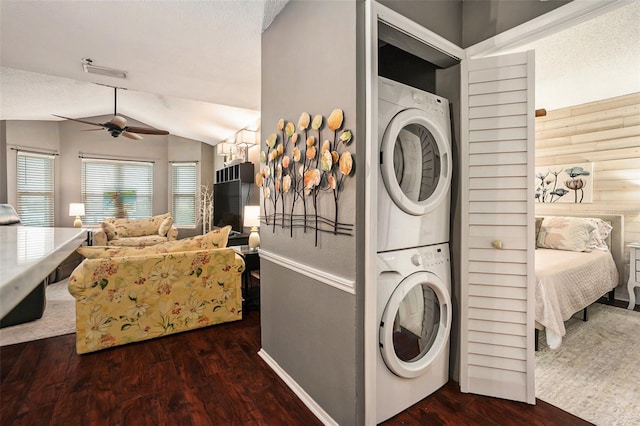 laundry area with wood walls, dark wood-type flooring, stacked washing maching and dryer, and ceiling fan