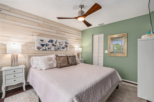 bedroom with a textured ceiling, rustic walls, wooden walls, a closet, and ceiling fan