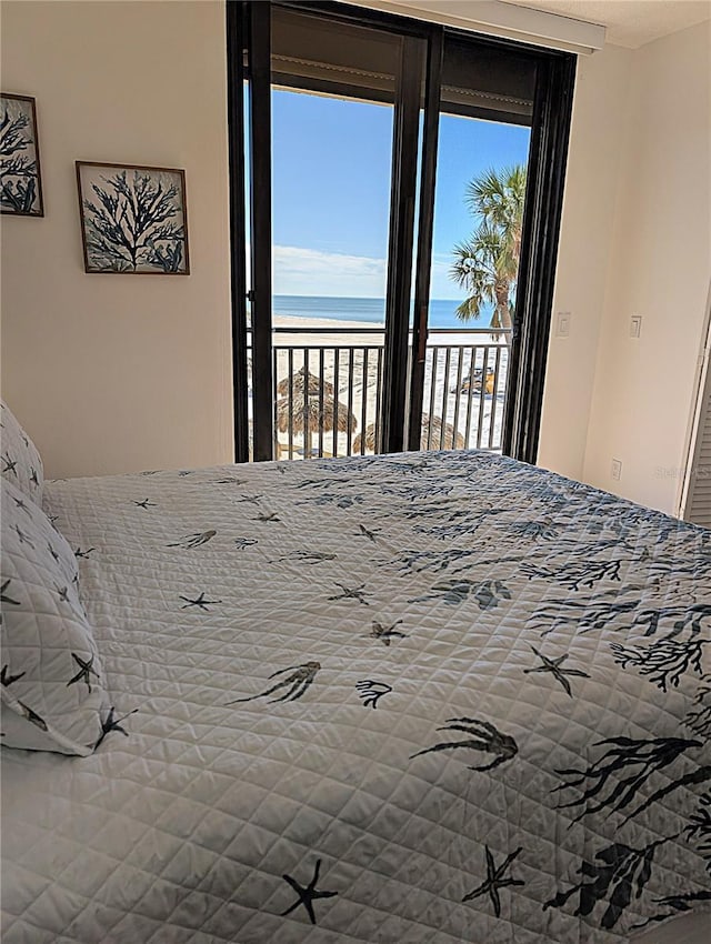 unfurnished bedroom featuring multiple windows, a water view, access to outside, and a beach view