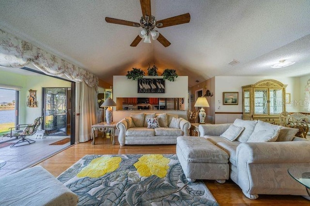 living room with lofted ceiling, hardwood / wood-style floors, a textured ceiling, and ceiling fan