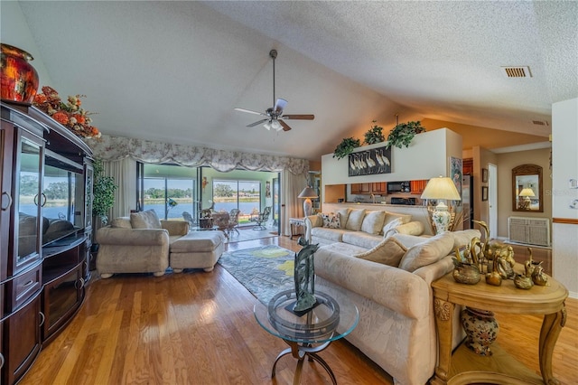 living room featuring lofted ceiling, a water view, a textured ceiling, light wood-type flooring, and ceiling fan