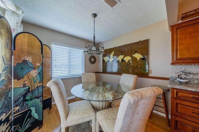 dining space featuring a notable chandelier, a textured ceiling, and light hardwood / wood-style flooring