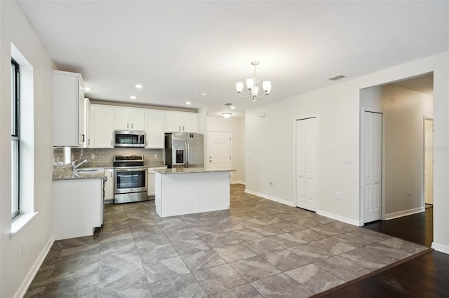 kitchen featuring pendant lighting, a center island, white cabinetry, stainless steel appliances, and light stone counters