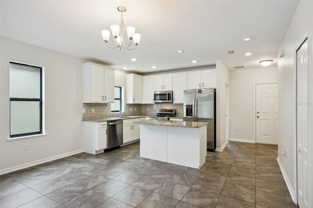 kitchen with white cabinets, appliances with stainless steel finishes, a center island, decorative light fixtures, and light stone counters