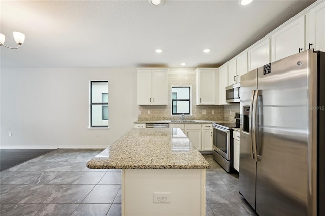 kitchen with a center island, sink, white cabinetry, light stone countertops, and appliances with stainless steel finishes