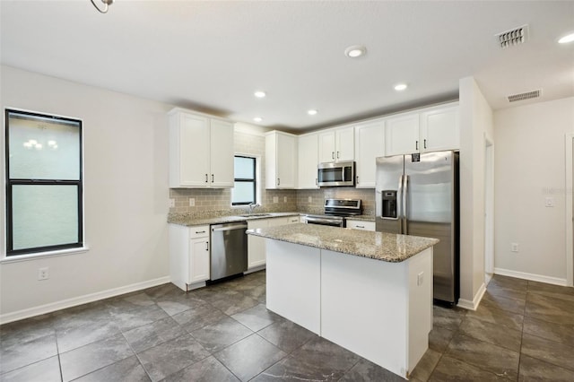 kitchen featuring light stone countertops, appliances with stainless steel finishes, a kitchen island, white cabinetry, and tasteful backsplash