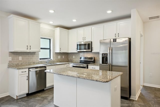 kitchen featuring white cabinetry, stainless steel appliances, backsplash, light stone counters, and a center island