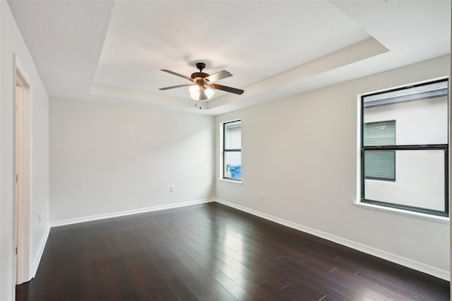 unfurnished room featuring ceiling fan, dark hardwood / wood-style floors, and a tray ceiling