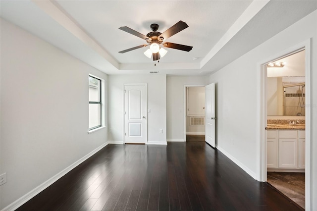 unfurnished bedroom featuring connected bathroom, dark hardwood / wood-style floors, a closet, ceiling fan, and a tray ceiling