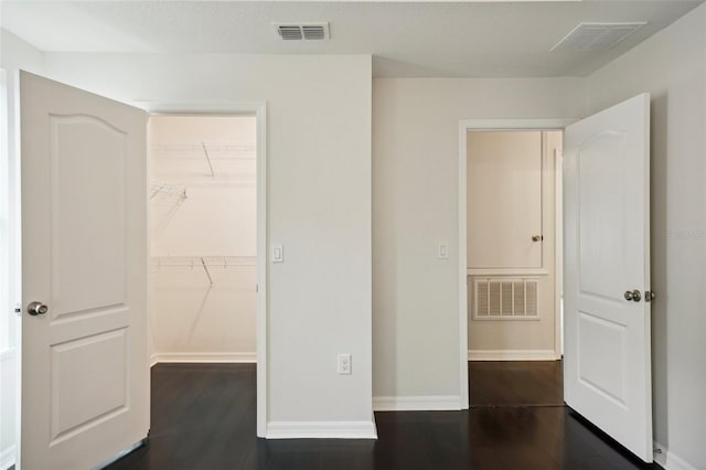 unfurnished bedroom featuring a closet, a spacious closet, and dark hardwood / wood-style floors