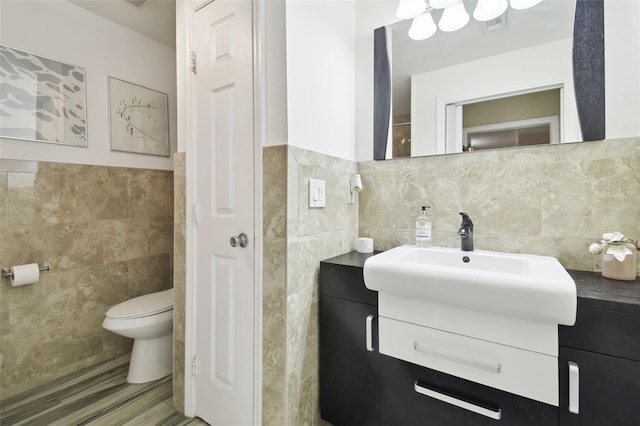 bathroom with wood-type flooring, toilet, vanity, and tile walls