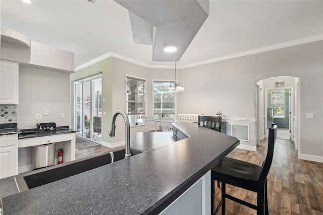 kitchen with a kitchen breakfast bar, ornamental molding, pendant lighting, and white cabinets