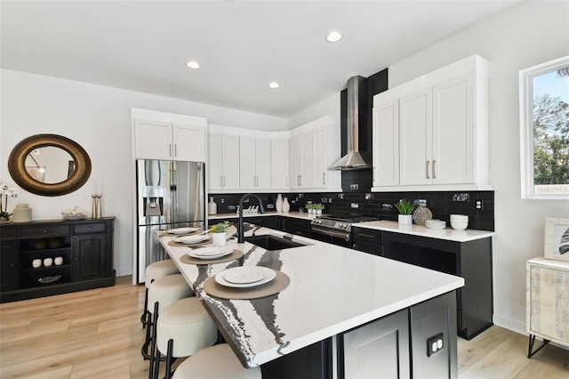 kitchen featuring appliances with stainless steel finishes, sink, a kitchen island with sink, and wall chimney range hood