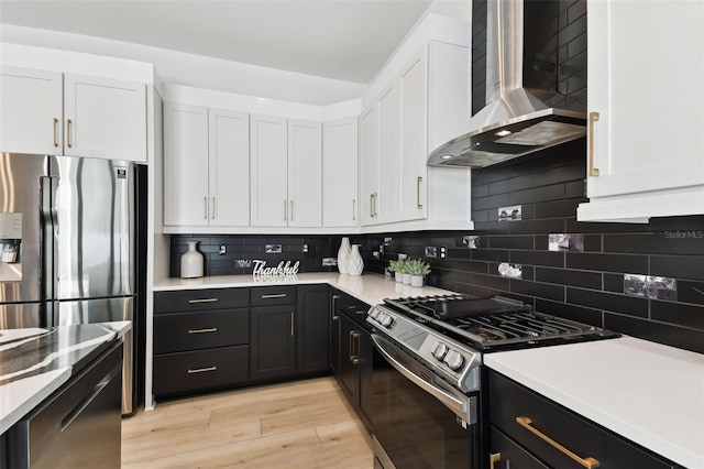 kitchen with white cabinetry, stainless steel appliances, tasteful backsplash, wall chimney exhaust hood, and light wood-type flooring