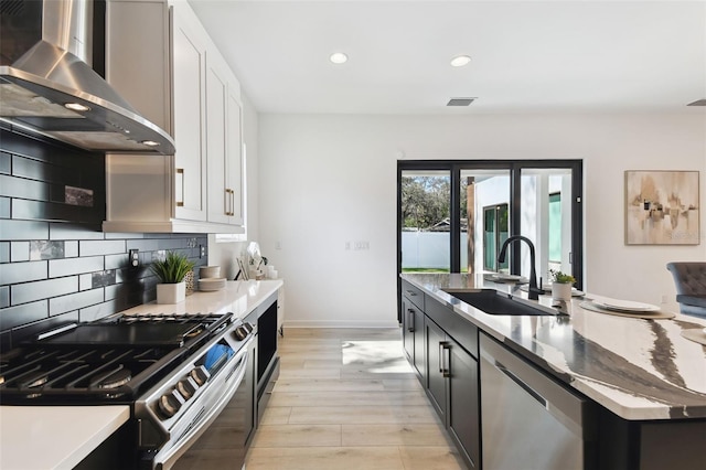 kitchen featuring sink, white cabinetry, wall chimney range hood, stainless steel appliances, and backsplash