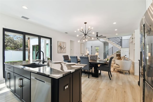 kitchen featuring pendant lighting, dishwasher, sink, light stone counters, and light wood-type flooring