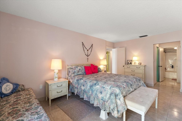 bedroom featuring ensuite bath, a textured ceiling, and light tile patterned floors