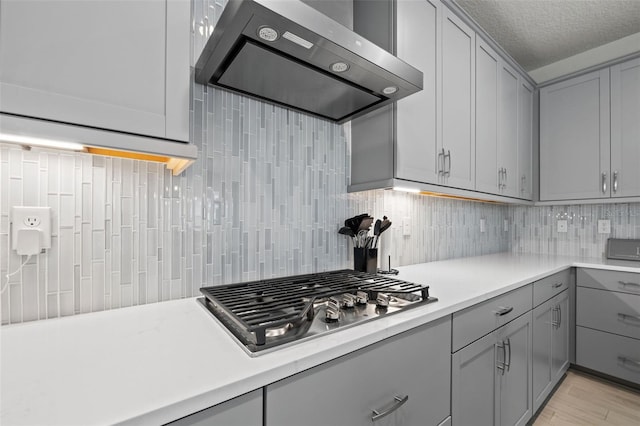 kitchen featuring backsplash, gray cabinetry, stainless steel gas stovetop, and wall chimney range hood