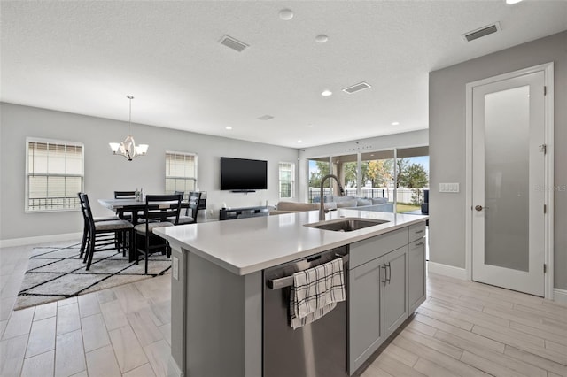 kitchen with stainless steel dishwasher, hanging light fixtures, sink, gray cabinetry, and a kitchen island with sink