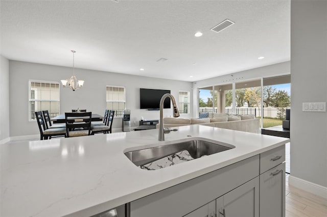 kitchen featuring hanging light fixtures, sink, light wood-type flooring, light stone countertops, and a chandelier