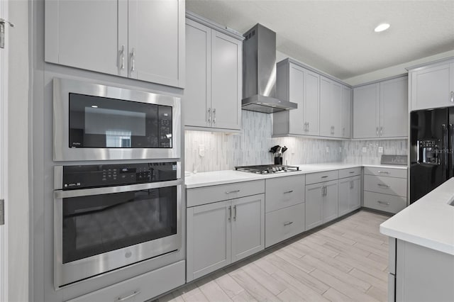 kitchen with stainless steel appliances, wall chimney exhaust hood, tasteful backsplash, and gray cabinets