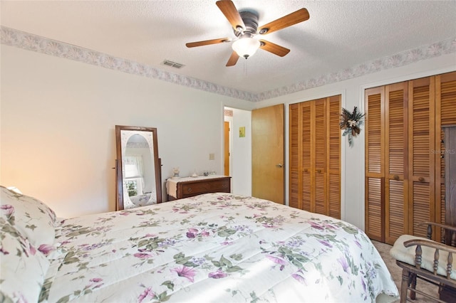 bedroom with two closets, a textured ceiling, and ceiling fan