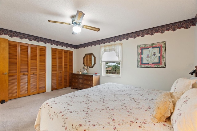 bedroom with light carpet, a textured ceiling, ceiling fan, and two closets