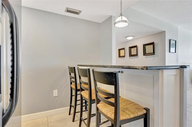 bar with hanging light fixtures, light tile patterned flooring, dark stone countertops, and a textured ceiling