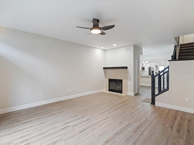 unfurnished living room featuring a tiled fireplace, ceiling fan, and light hardwood / wood-style flooring