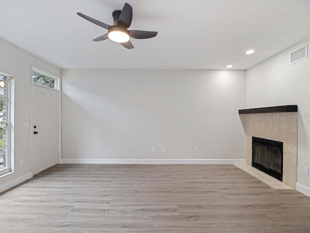 unfurnished living room with ceiling fan, a tiled fireplace, and light hardwood / wood-style floors