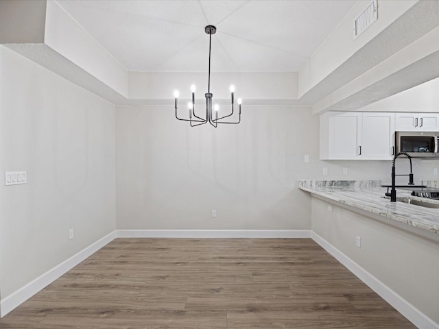 unfurnished dining area featuring a tray ceiling, sink, a chandelier, and hardwood / wood-style floors