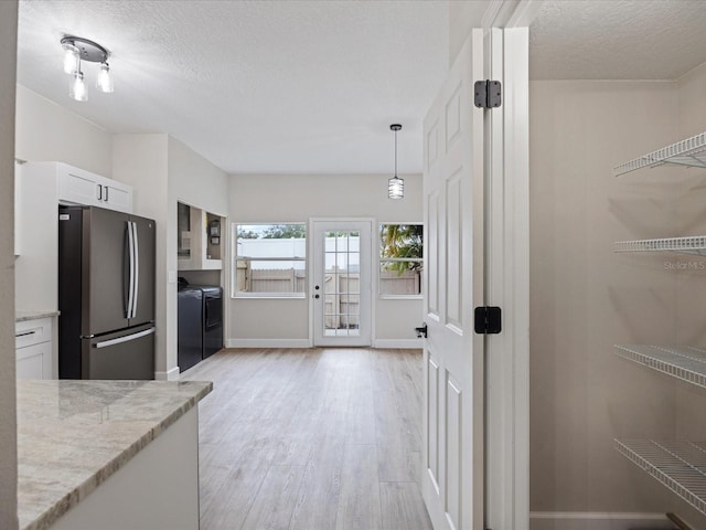 kitchen featuring white cabinetry, washer and dryer, stainless steel refrigerator, pendant lighting, and light stone countertops